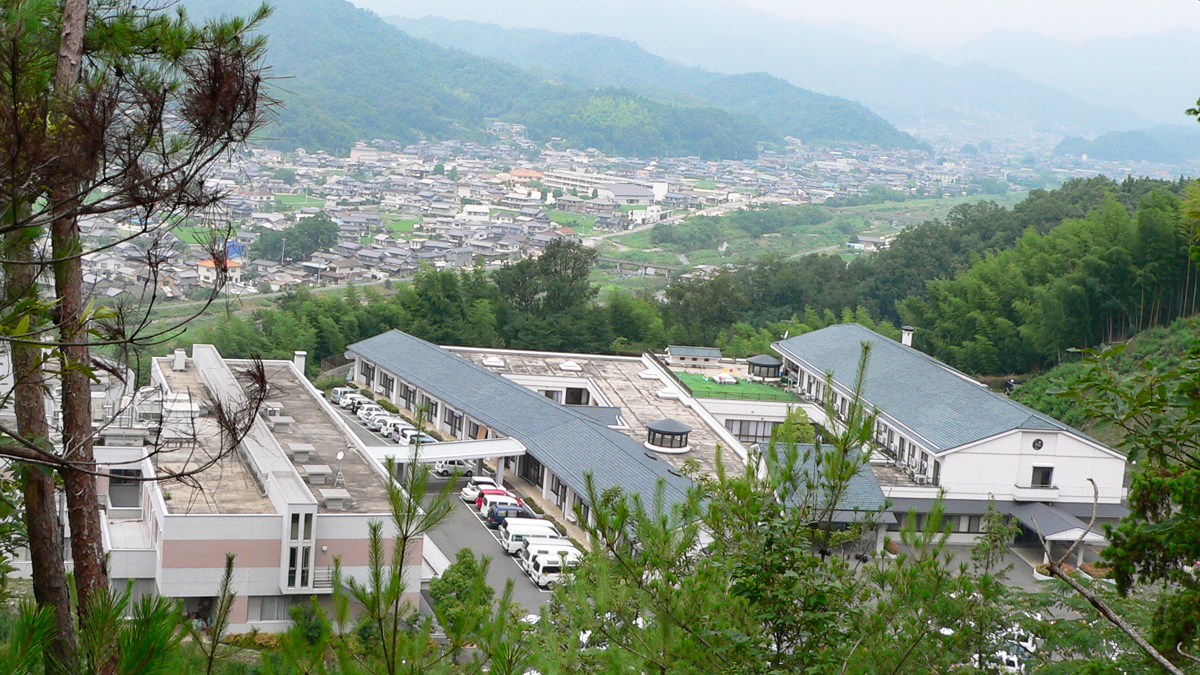 山間の介護施設の外観。谷間に位置する複合建物群が見える。
